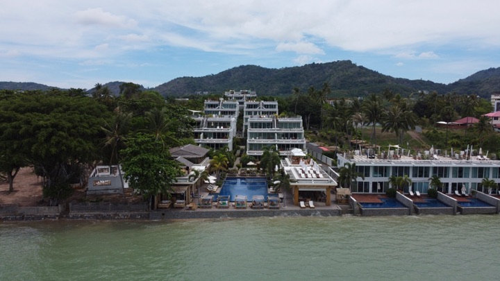 White hotel buildings with a pool on a green hillside seen from the water