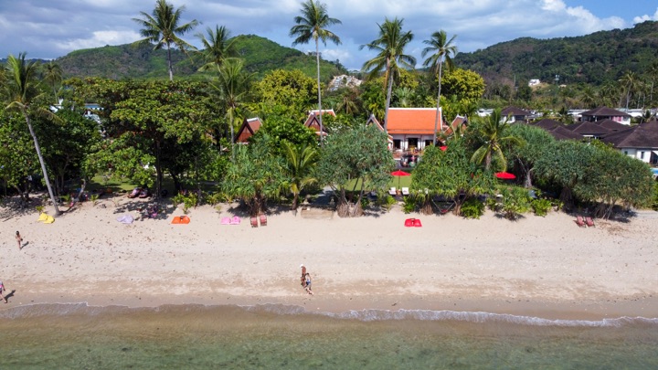Aerial view of a palm-fringed beach resort with a sandy shore and turquoise shallows