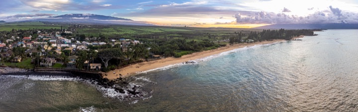 Aerial panorama of a coastal town and a curving sandy beach at dusk, with a cloud-capped mountain behind