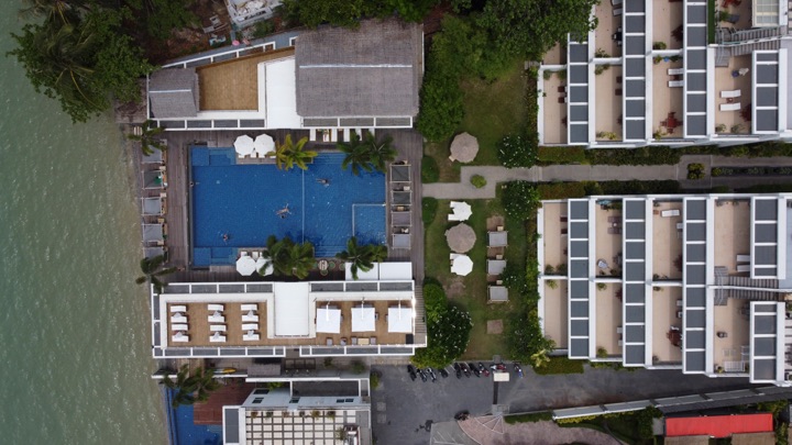 Aerial top-down of a hotel pool nestled between two accommodation blocks and gardens