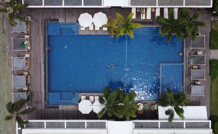 Top-down aerial of a deep blue swimming pool lined with palms and white loungers