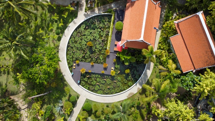 Top-down aerial of a circular lotus pond beside terracotta-roofed villas in dense greenery