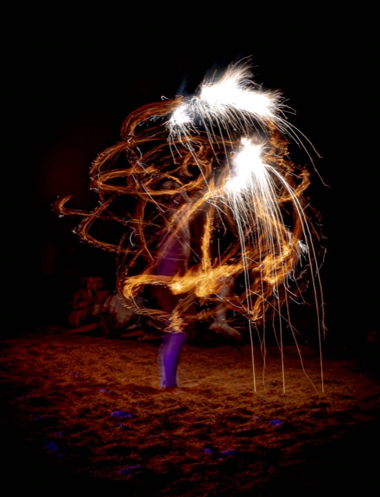 Performer spinning fire poi at night, leaving swirling trails of sparks