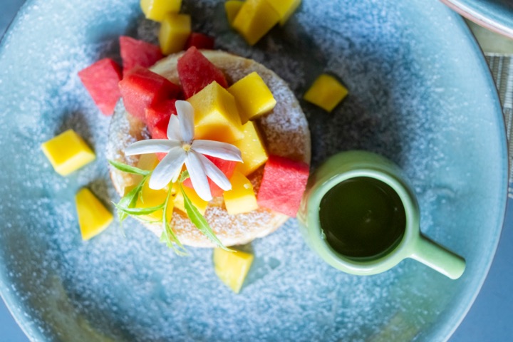 Pancakes topped with fresh mango and watermelon cubes, served with a small jug of green syrup