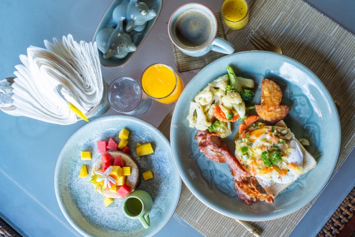 Top-down view of a breakfast table with two plates, orange juice and a cup of coffee on a rattan mat