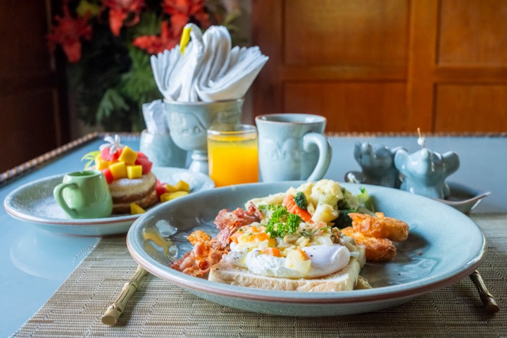 Eggs benedict with bacon on a blue plate, with orange juice and napkins in the background
