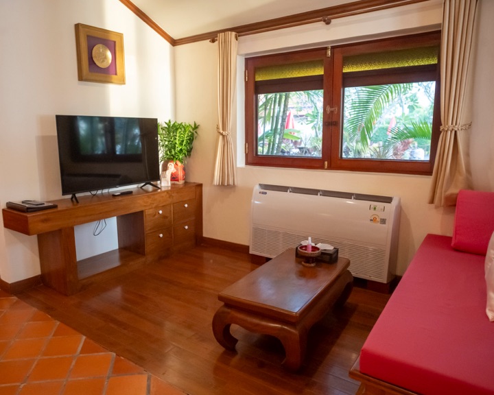Villa sitting room with a red daybed, a carved coffee table and a window onto palm gardens
