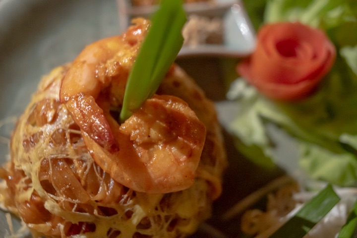 Close-up of prawns on a nest of noodles wrapped in an egg lattice, garnished with a tomato rose
