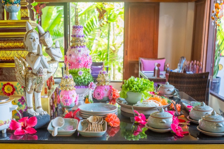 Restaurant display of celadon tableware, tropical flowers and traditional floral arrangements beside a Thai angel statue