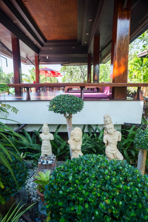 Open-air resort lounge with carved stone figures and a clipped topiary tree in the foreground
