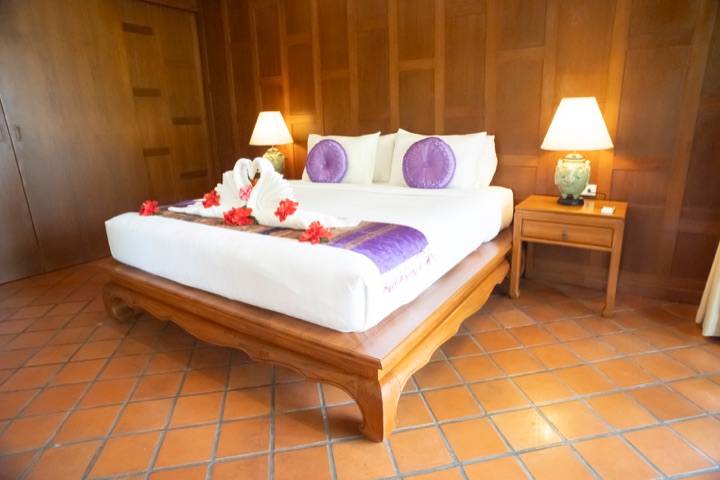 Bed with a purple runner, towel swans and red hibiscus flowers in a teak-panelled room