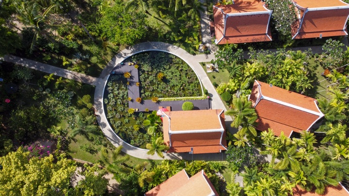 Top-down aerial of a circular lotus pond with a wooden deck and potted plants beside orange-roofed villas