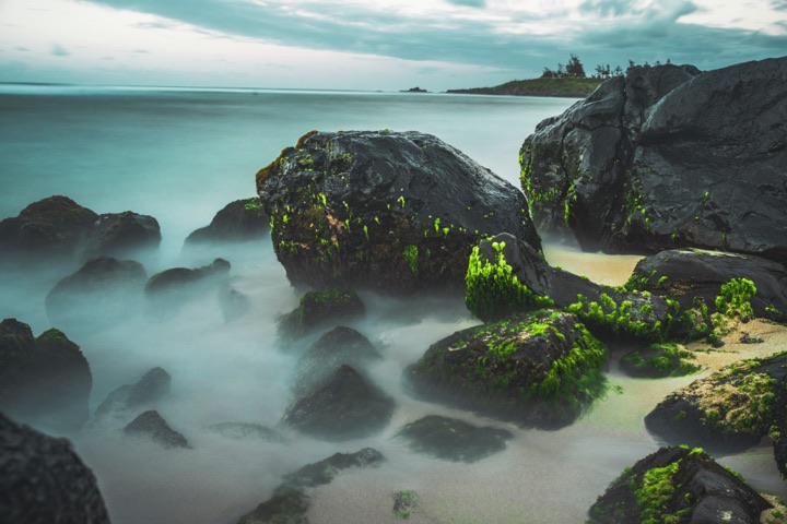 Long-exposure of moss-covered boulders on a misty beach at dawn