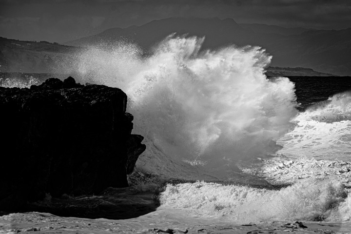Black and white photograph of a wave crashing against a rock shelf