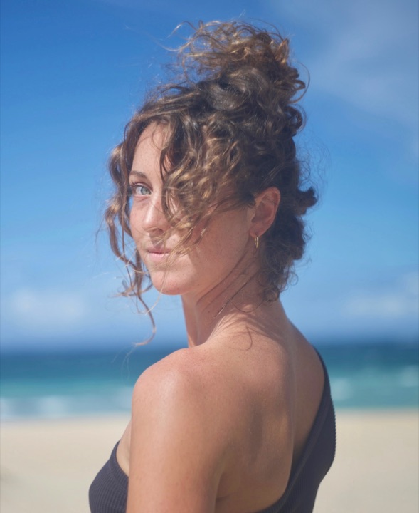 Woman with curly hair glancing over her shoulder on a windy beach