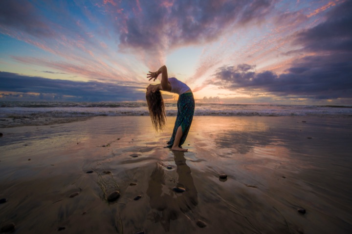 Dancer arching backward on a wet beach reflecting a fiery sunset sky