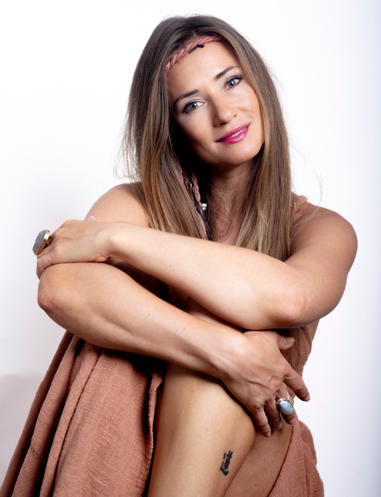 Woman wrapped in terracotta linen hugging her knees, seated against a white studio backdrop