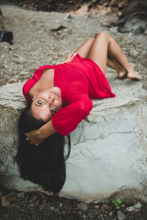 Woman in a red dress lying on a pale boulder, looking at the camera