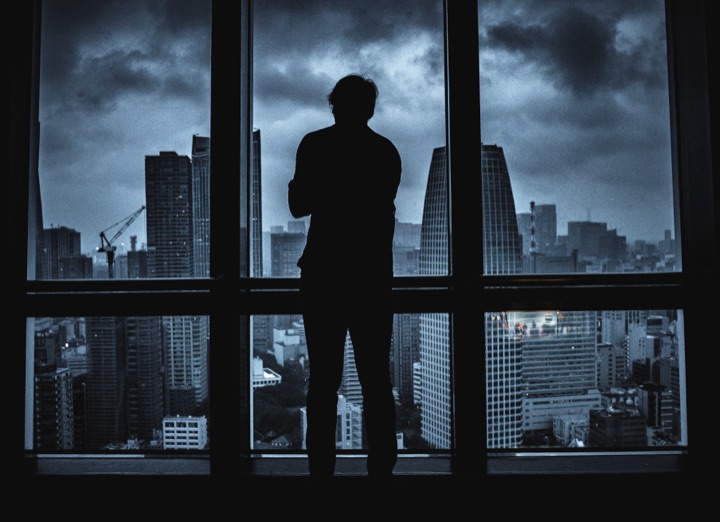 Silhouette of a man standing at a window overlooking a stormy city skyline