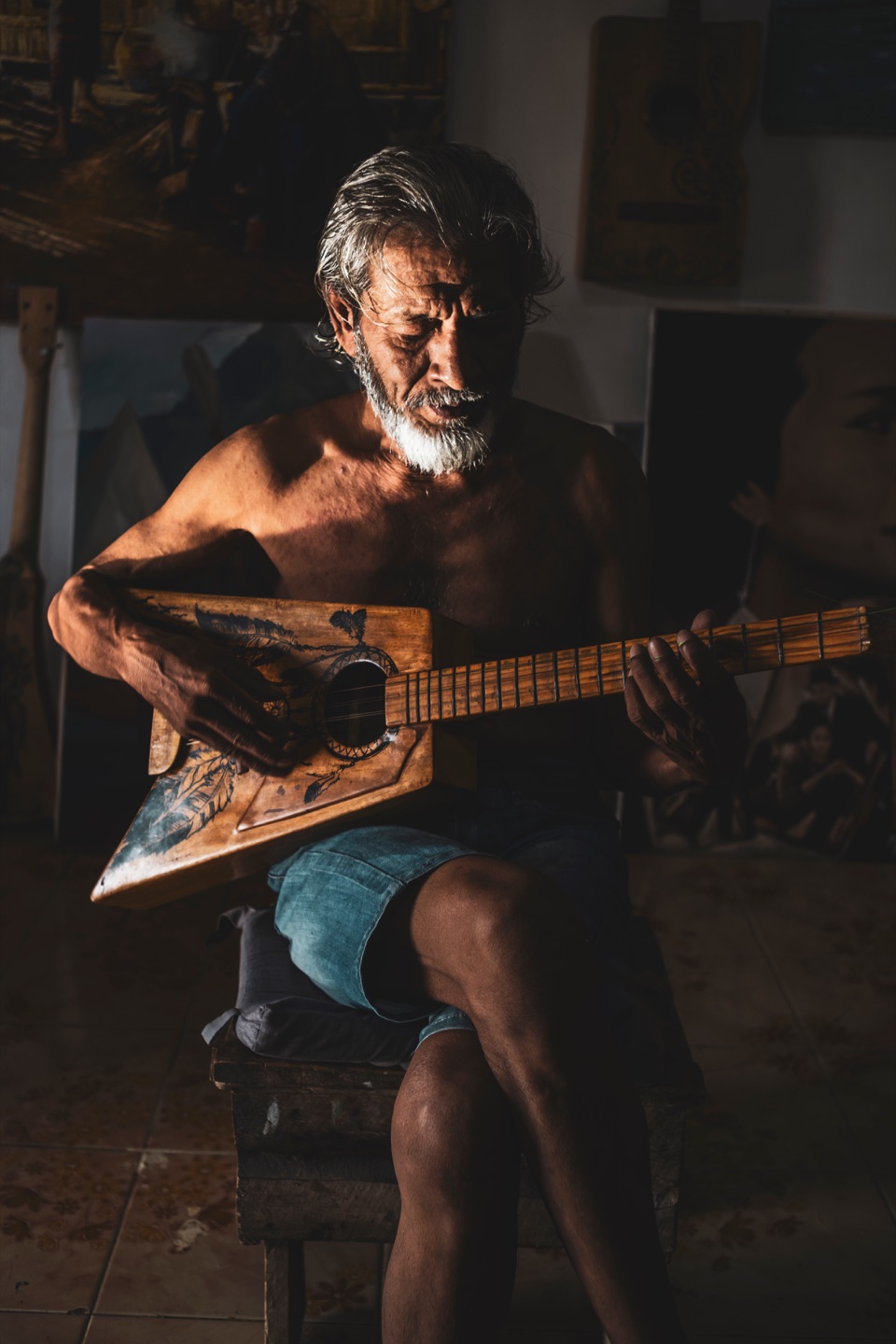 Bearded man playing a hand-carved guitar in warm lamplight