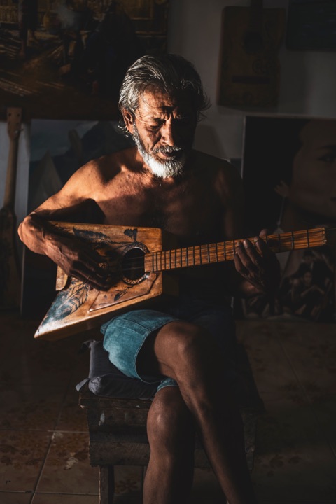 Bearded man playing a hand-carved guitar in warm lamplight