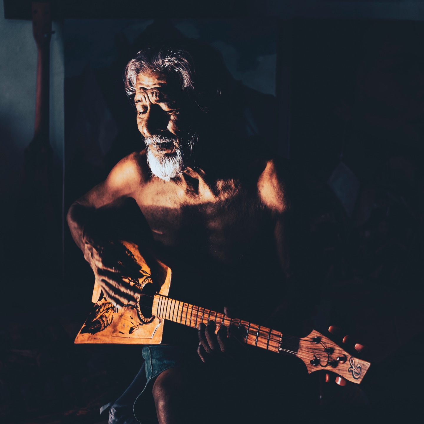 Man holding a carved guitar, dramatically side-lit against darkness