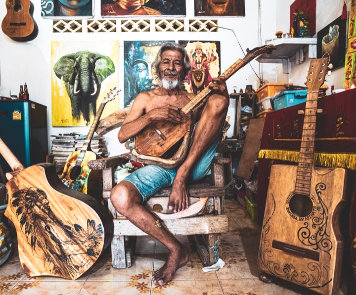 Artist seated among paintings and guitars in a cluttered studio