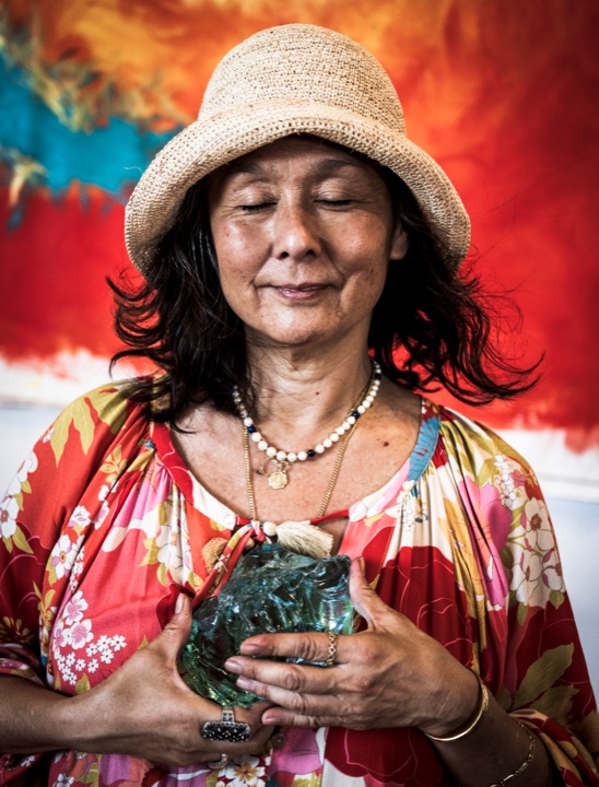 Woman in a straw hat and floral dress holding a sculpture with her eyes closed