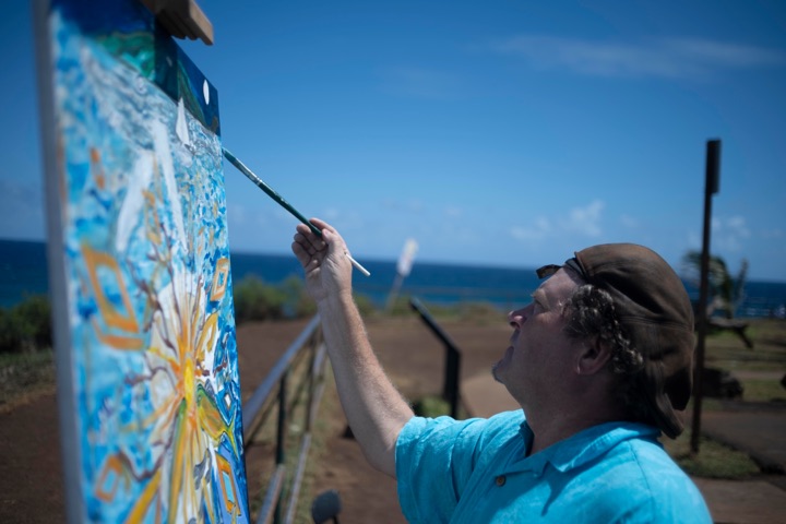 Painter working at an easel outdoors on a bluff above the sea