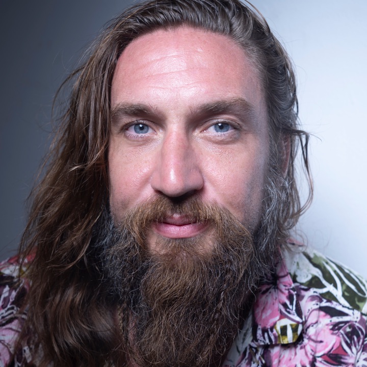 Close-up of a bearded man in a floral shirt looking calmly at the camera