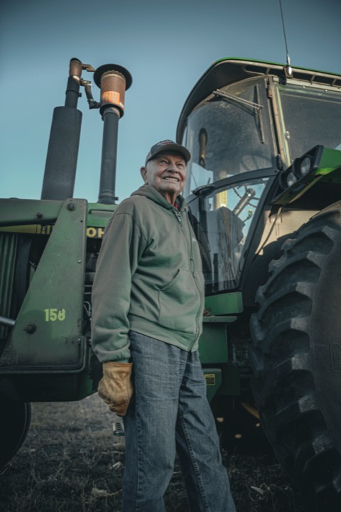 Man in a cap standing beside a green tractor