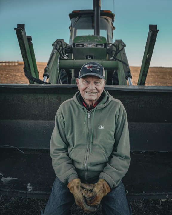 Smiling man in a hoodie and work gloves in front of a tractor