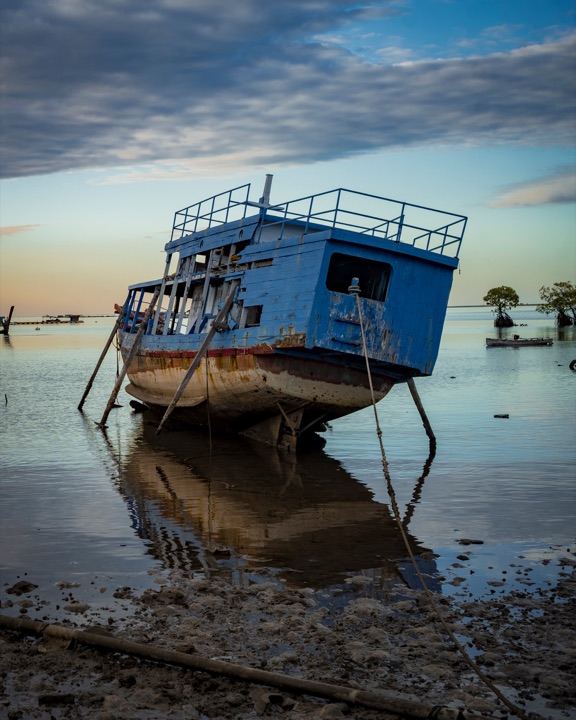 Blue fishing boat resting on a sandy shore at sunset