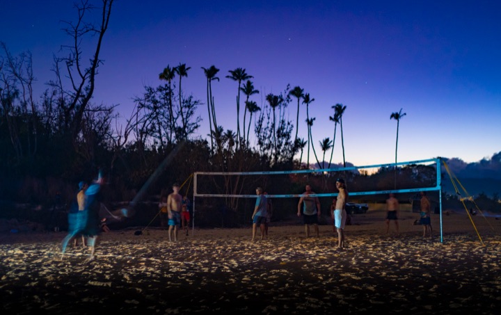 People playing beach volleyball at dusk under palm trees
