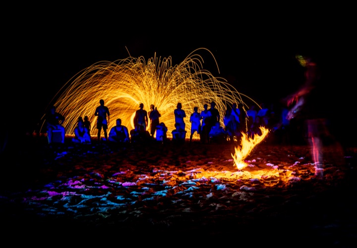 Crowd silhouetted against a shower of sparks at a beach fire show
