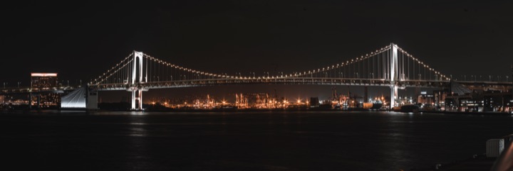 Panorama of an illuminated suspension bridge over dark water
