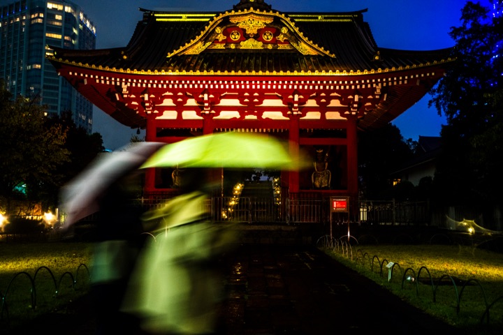 Red temple gate at night with a passer-by carrying a glowing green umbrella