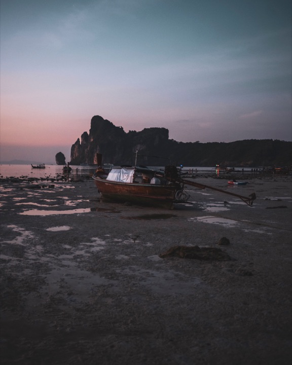 Longtail boat on a tidal flat at sunset with limestone cliffs behind