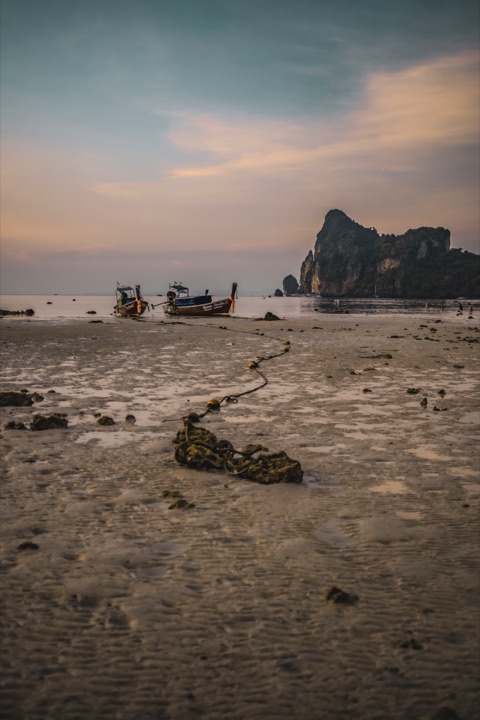 Boats on a tidal flat at sunset with a rocky headland