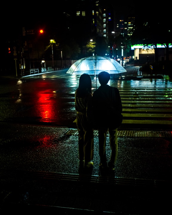 Couple sharing an umbrella at a rainy night crossing