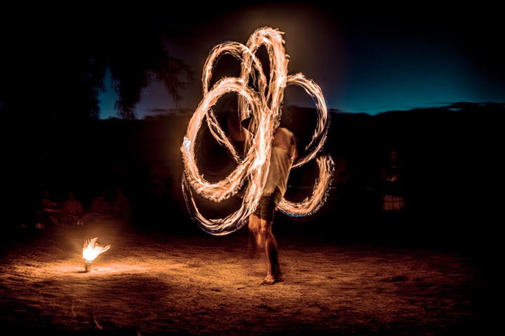 Fire poi spinner creating loops of light on a beach at night
