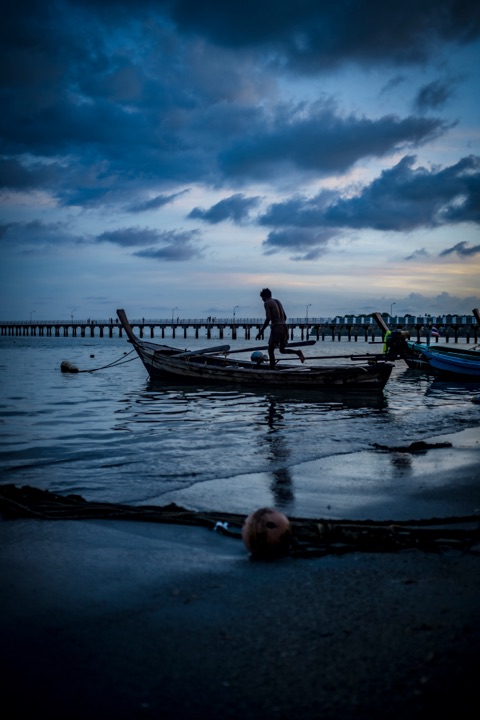 Longtail boat beside a pier under a stormy dusk sky